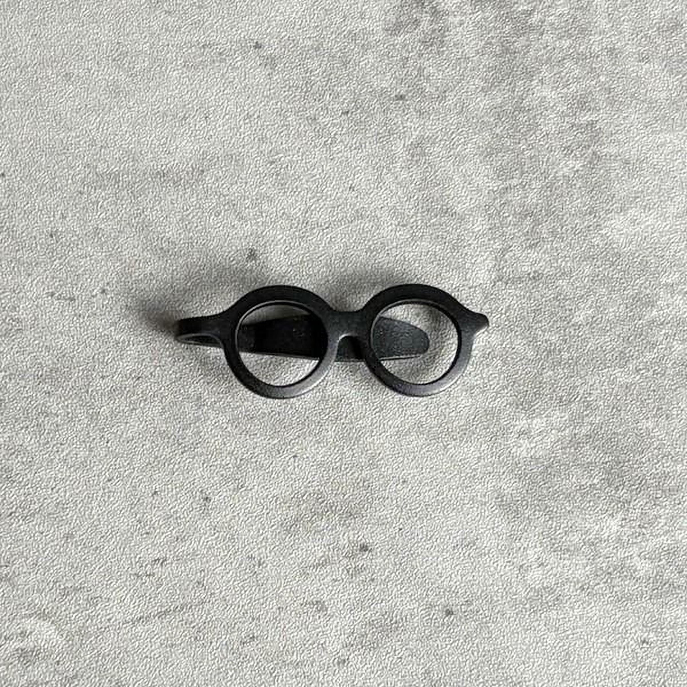 A pair of black glasses is placed on a textured gray surface.