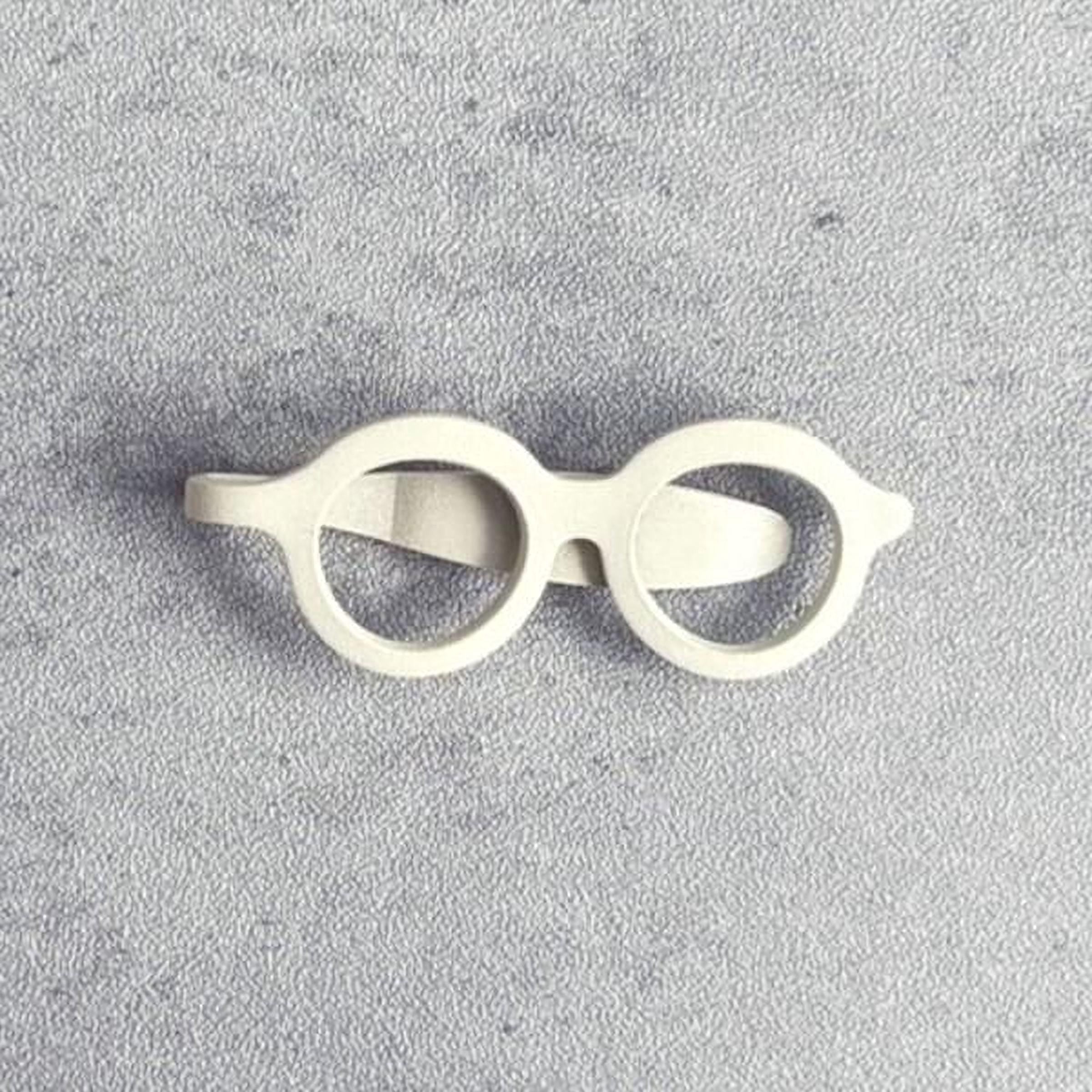 A pair of white, round-framed glasses is shown against a textured gray background.