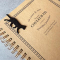 a spiral-bound notebook with a black cat figurine on the cover.