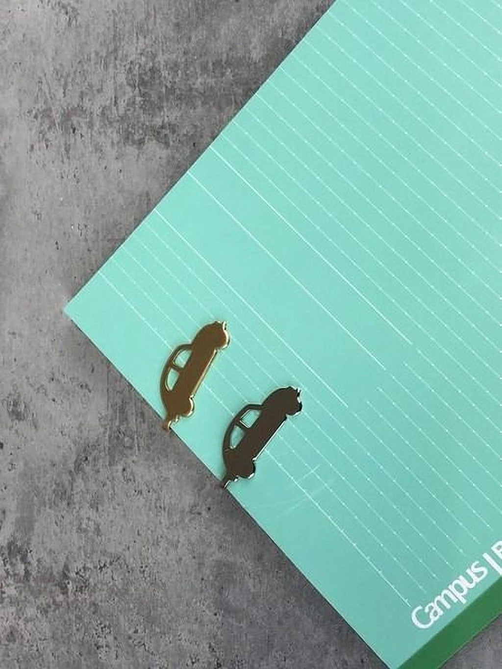 two gold car-shaped bookmarks placed on a green lined paper.