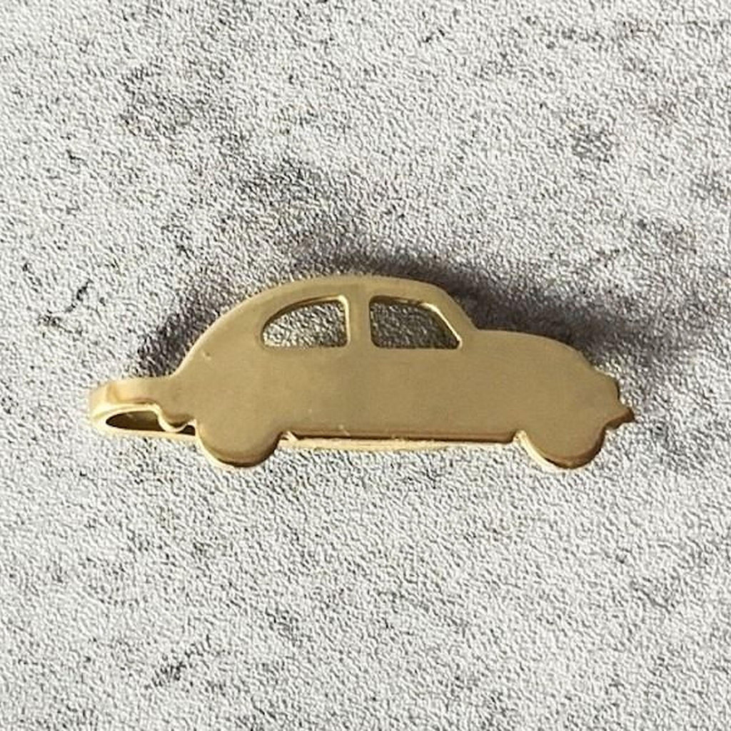A gold-colored car-shaped pendant or charm is shown against a textured gray background.
