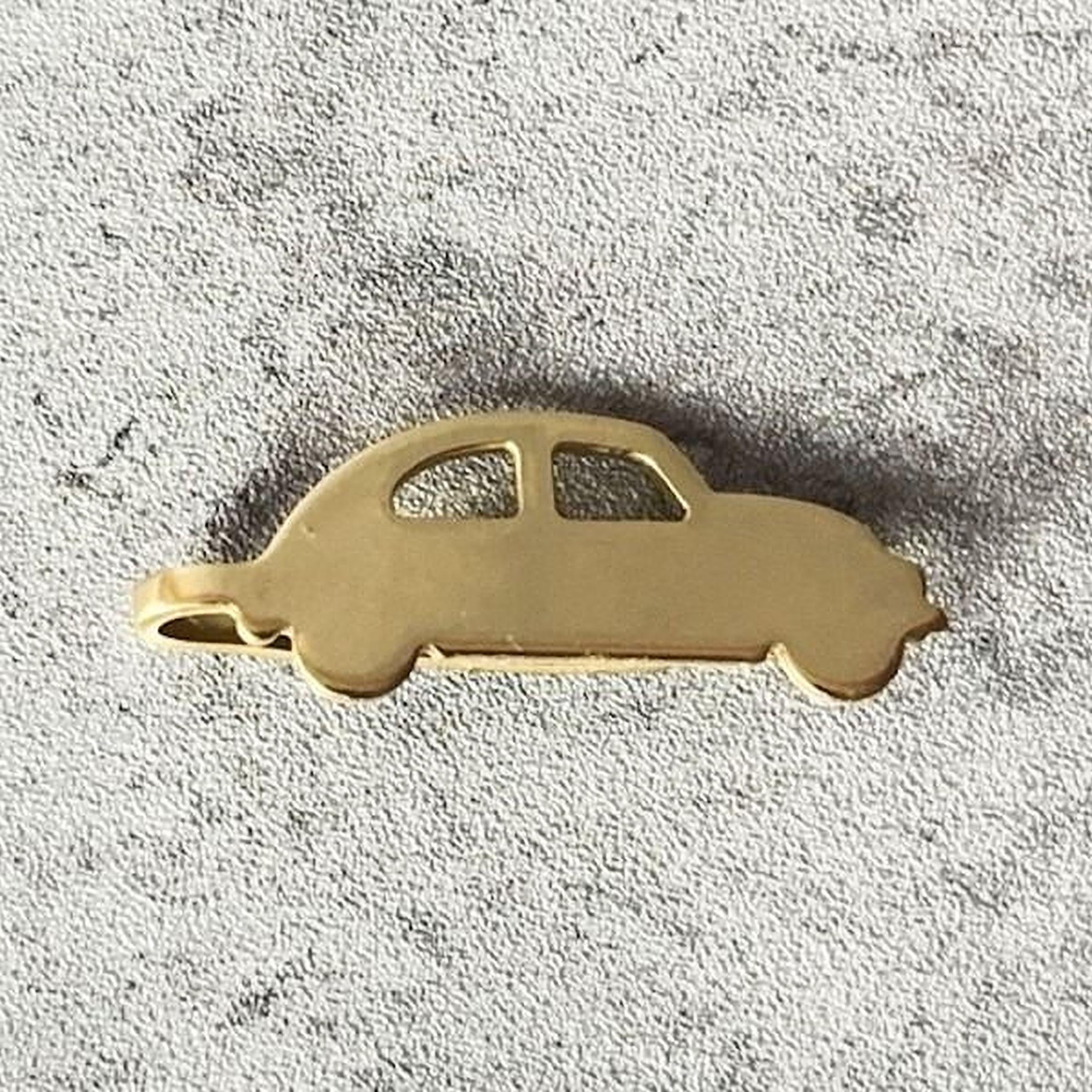 A gold-colored car-shaped pendant or charm is shown against a textured gray background.