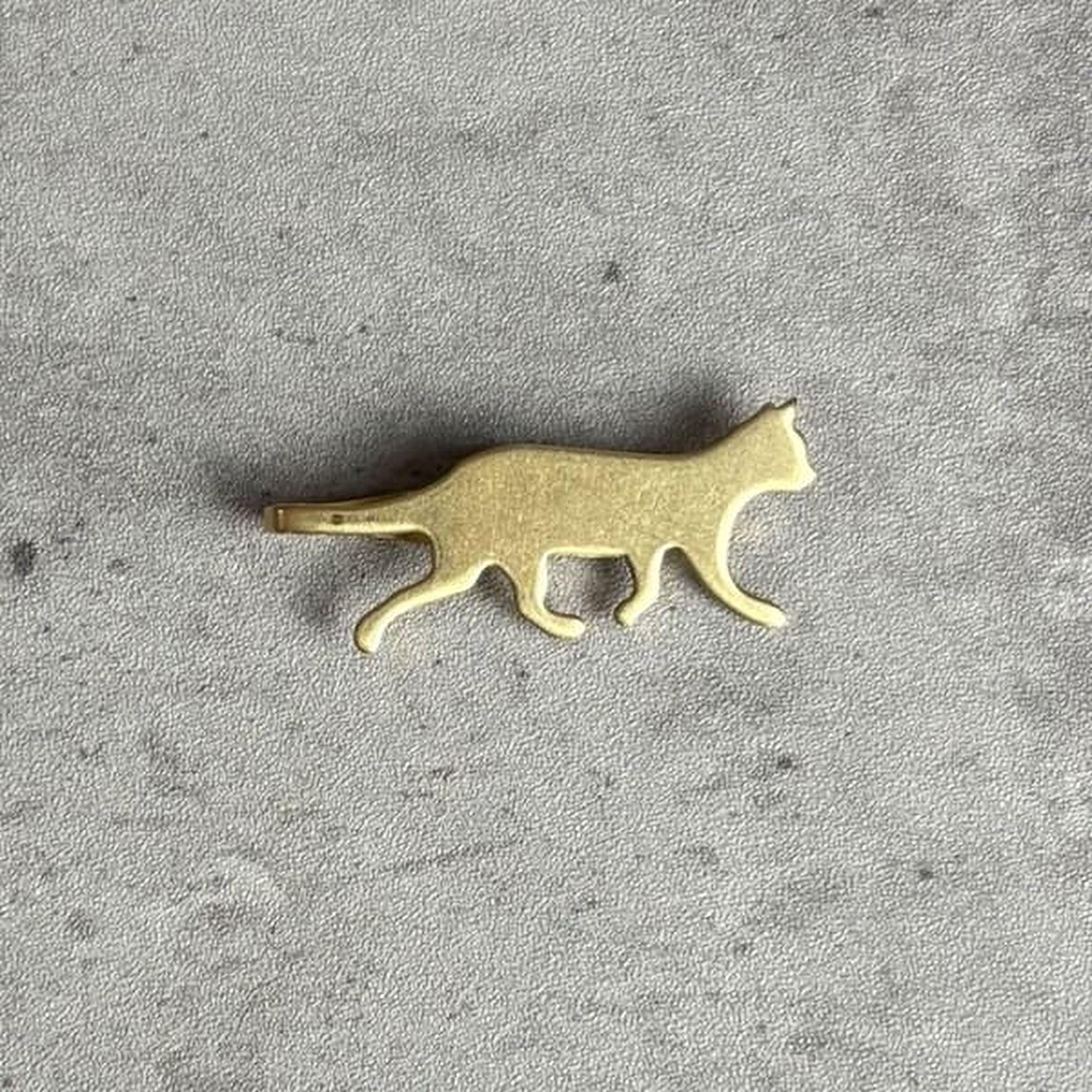 A small golden cat figurine is shown against a textured gray background.