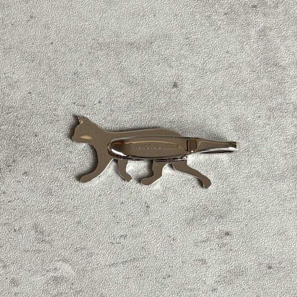 A silver-colored metal object resembling a cat is shown on a textured gray surface.
