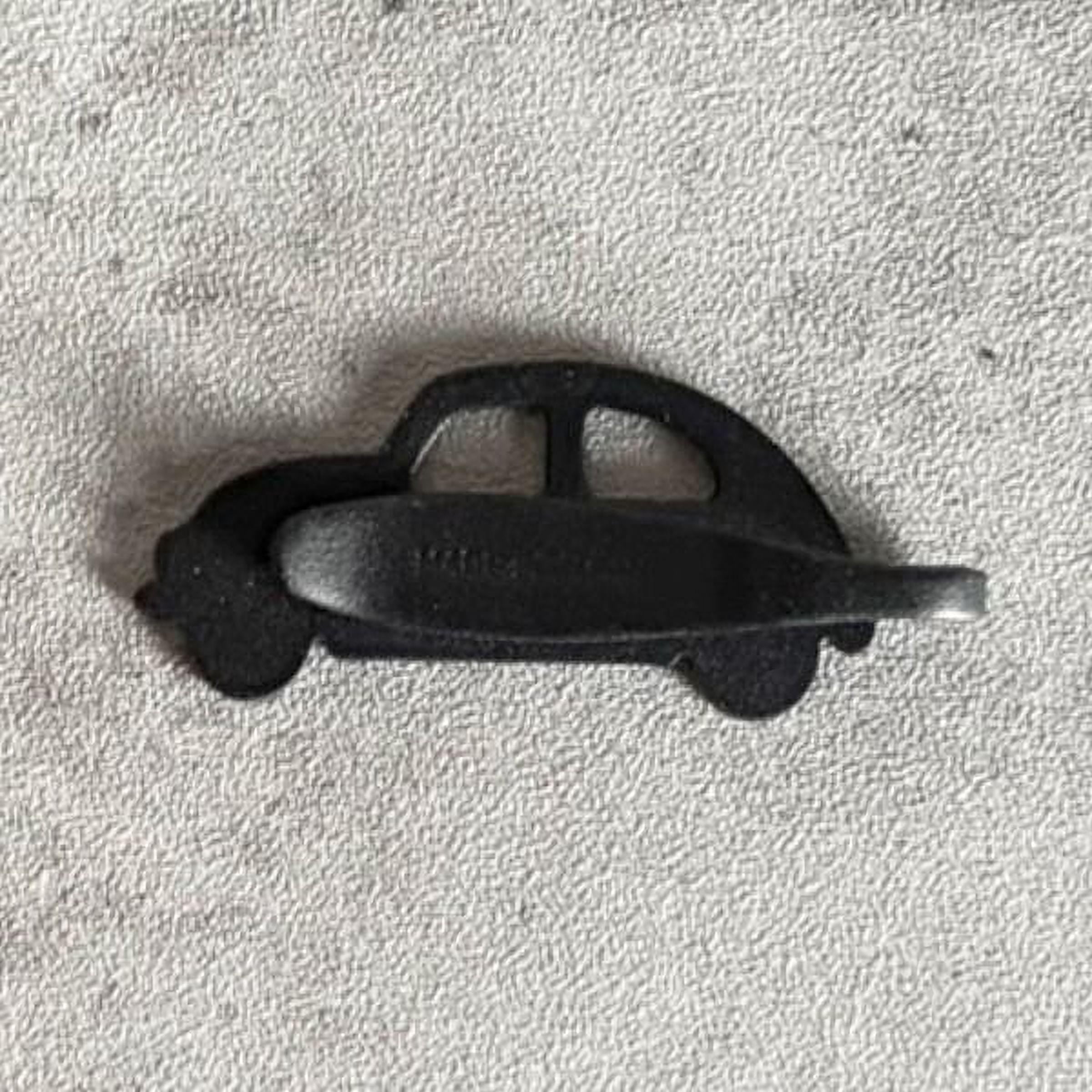 A black metal object resembling a car or automobile is shown on a textured surface.