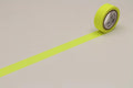 A roll of yellow tape with a black label is lying on a white surface, with a yellow line drawn on the surface.