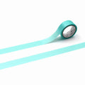 A roll of turquoise-colored tape is lying on a white surface, with a single blue line extending from the tape.