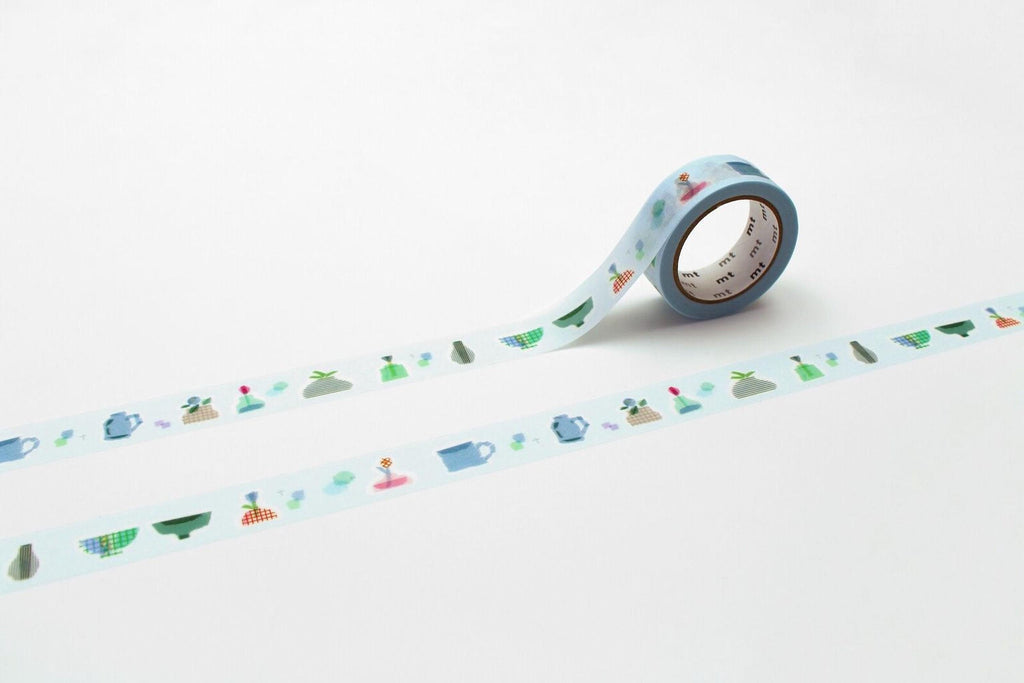 A roll of blue and white patterned tape with various objects such as cups, bowls, and plants printed on it, lying on a white surface.