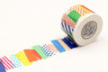 A roll of colorful tape with a pattern of various shapes and colors, including polka dots, stripes, and geometric designs, is shown on a white background.