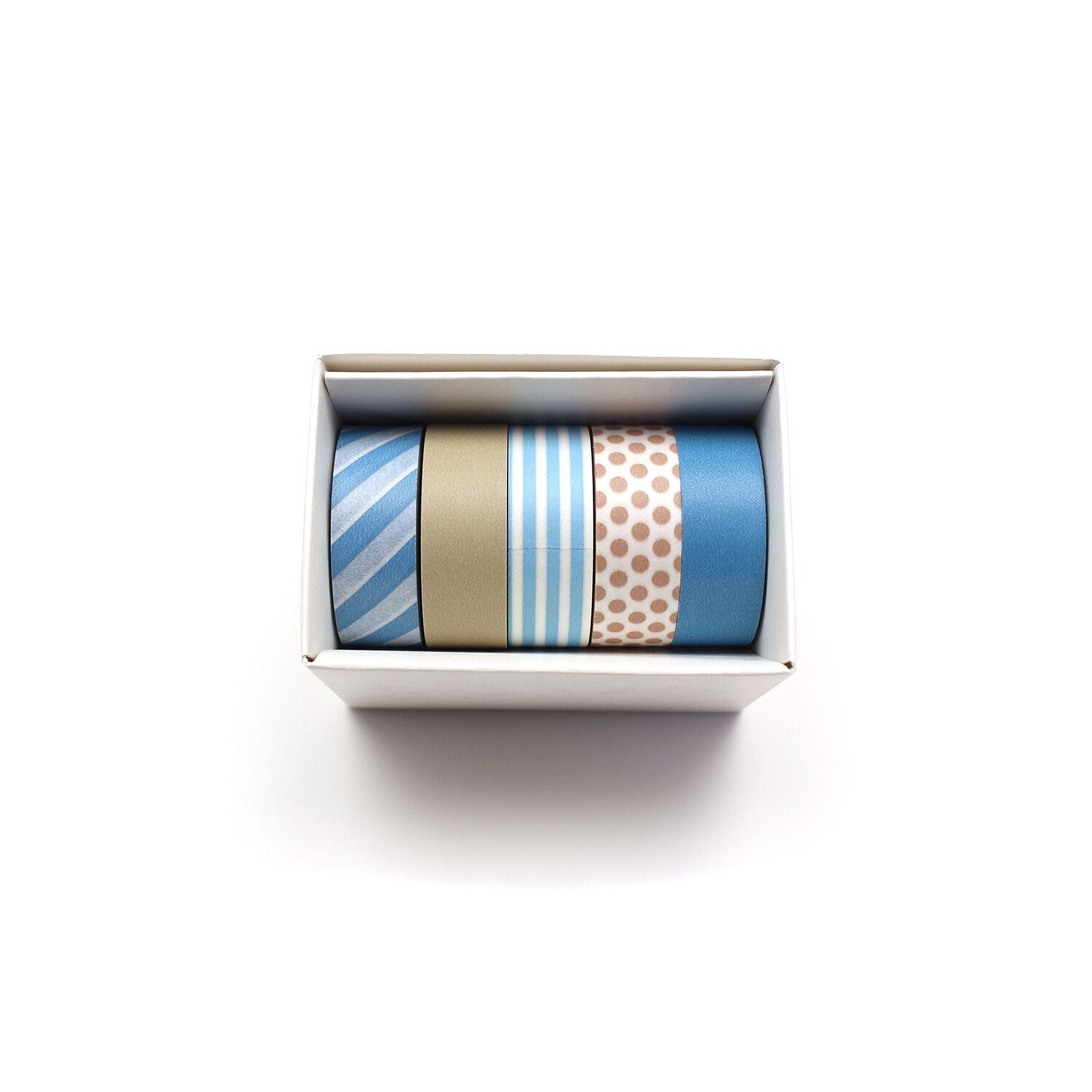 A white box containing four rolls of colorful tape in various patterns, including stripes, polka dots, and solid colors.