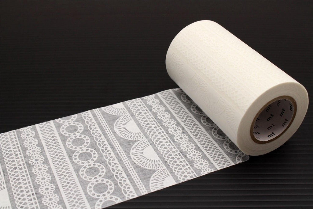 A roll of white toilet paper with a decorative lace pattern on it, placed on a black surface.