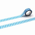 A roll of blue and white checkered tape is lying on a white surface, with the tape partially unspooled and extending across the image.