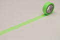 A roll of green tape with a white pattern on it is lying on a white surface, with a green line drawn on the surface.