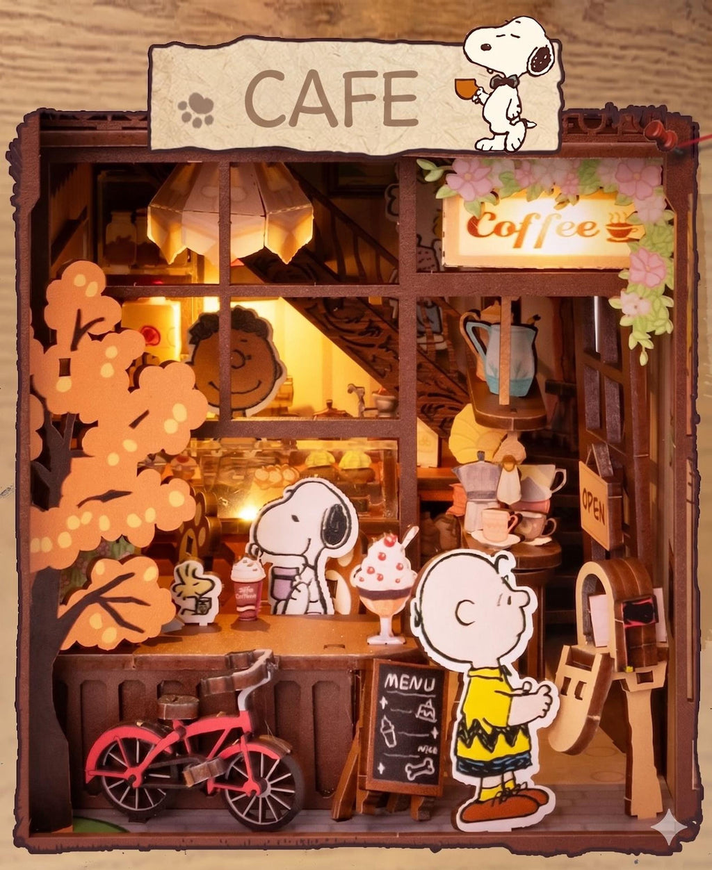 A charming miniature cafe scene featuring the iconic cartoon characters from the Peanuts comic strip, including Snoopy and Charlie Brown, with a bicycle and various cafe items and decorations.