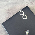 A pair of white glasses is placed on top of a black surface, with a small, colorful space-themed sticker or decal below it.