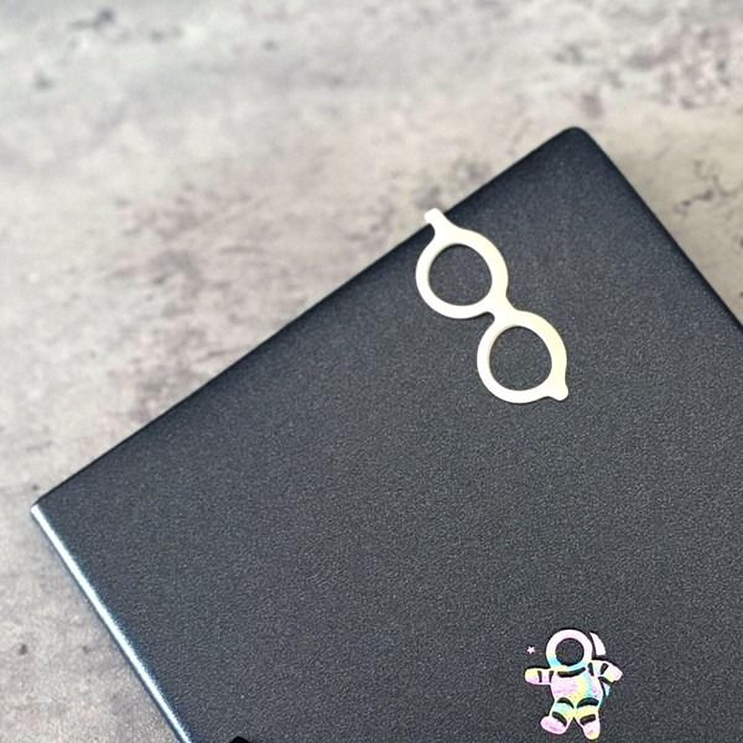 A pair of white glasses is placed on top of a black surface, with a small, colorful space-themed sticker or decal below it.