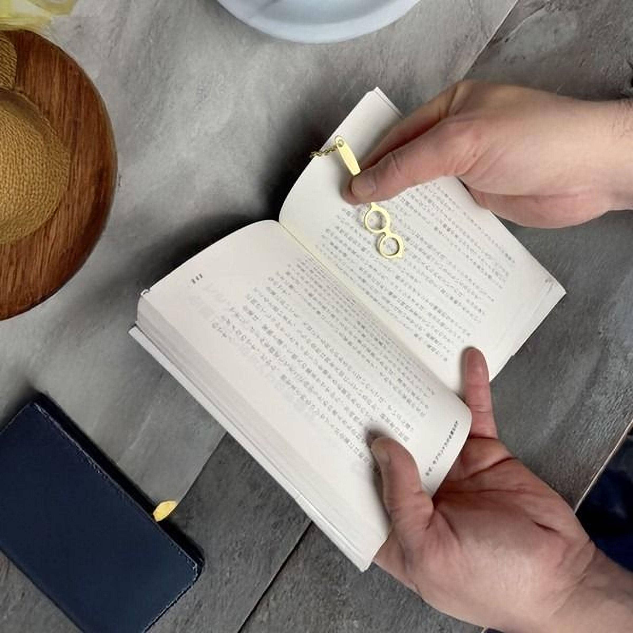 A person's hands holding an open book with text in a foreign language, and a gold-colored keychain or charm attached to the pages.