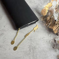 A black wallet or purse with a gold cat-shaped bookmark attached to it, along with some dried flowers and a dried leaf on a gray surface.