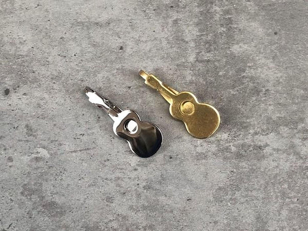 Two small, metallic guitar-shaped clips are placed on a gray surface.