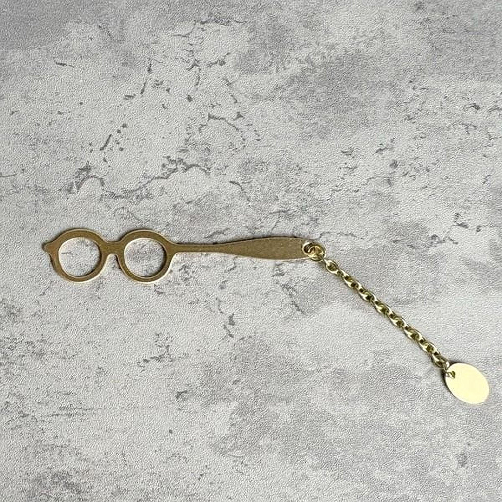 A pair of gold-colored metal scissors with a chain attached to the handle, resting on a textured gray surface.