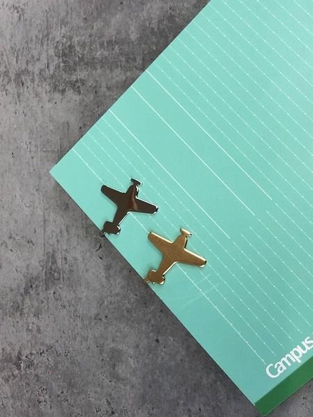 two small airplane-shaped clips on a green notebook with white lines.