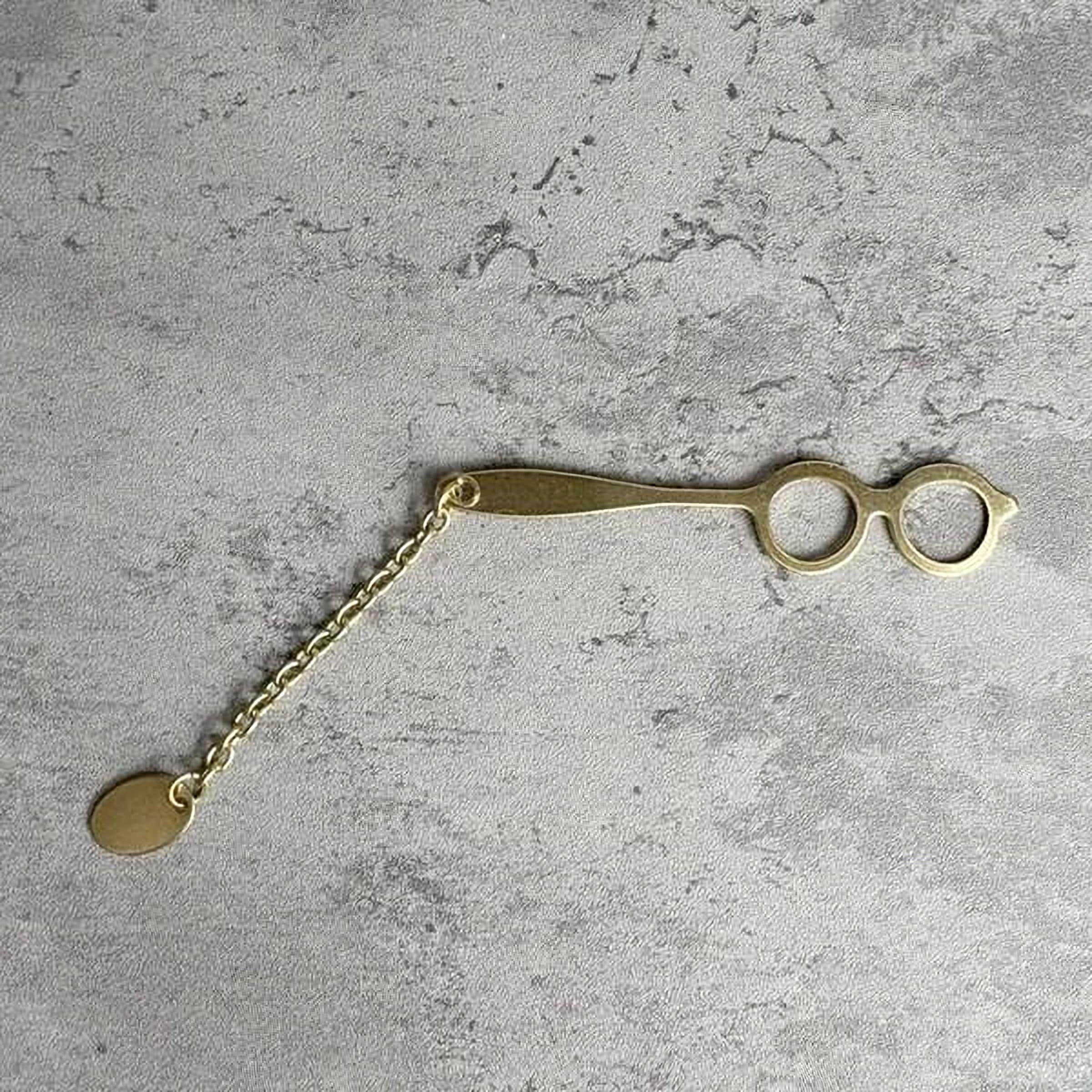 A pair of gold-colored metal scissors with a chain attached to them, resting on a textured gray surface.