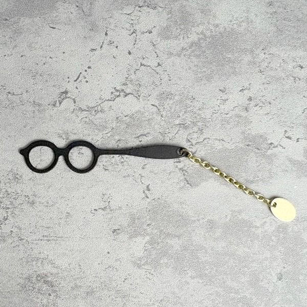 A pair of black glasses with a gold chain attached to them, resting on a textured gray surface.