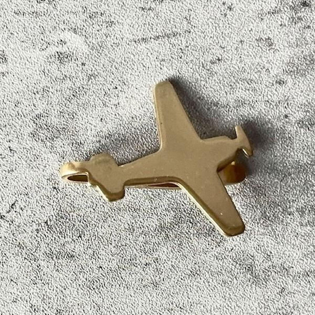 A small gold-colored airplane charm is resting on a textured gray surface.