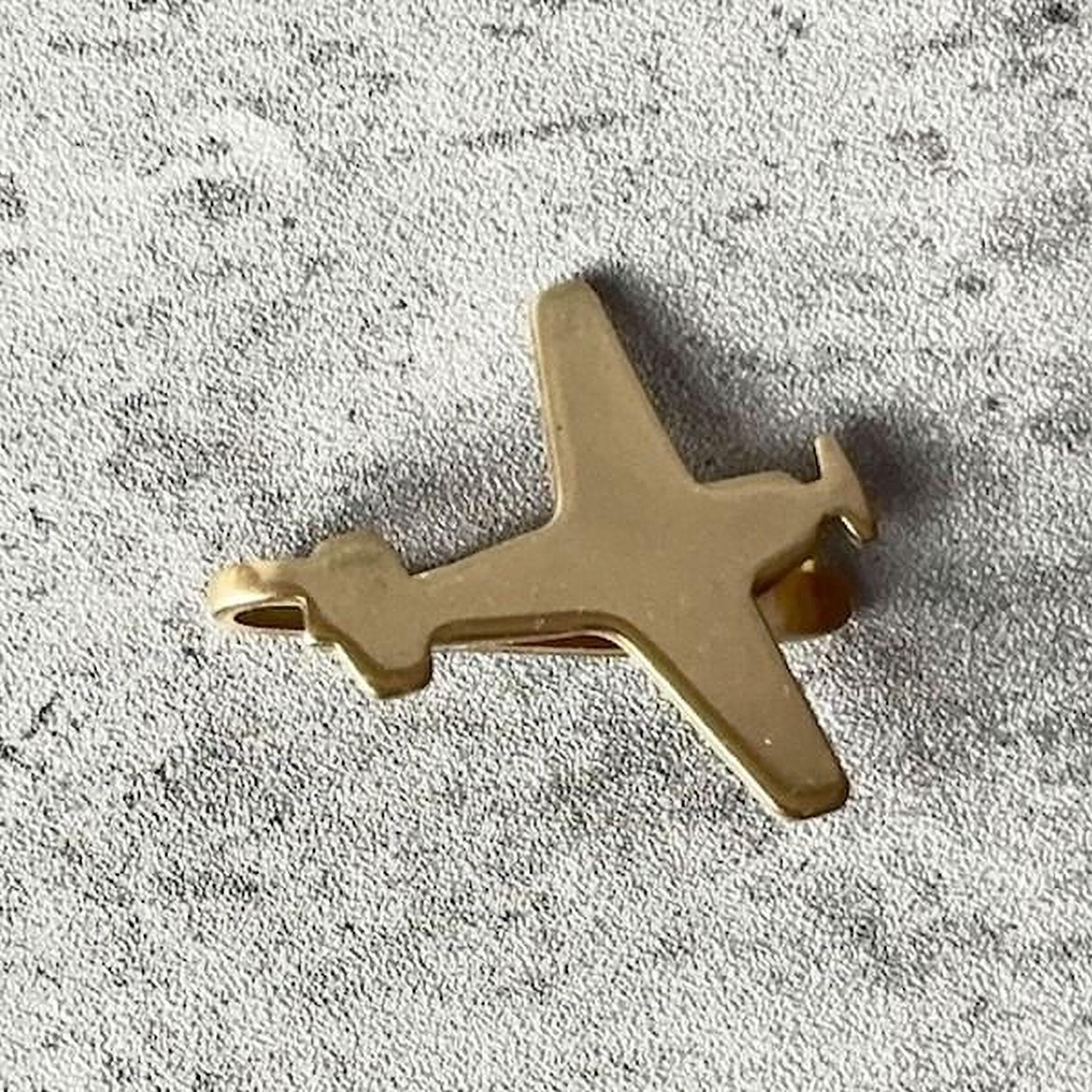 A small gold-colored airplane charm is resting on a textured gray surface.