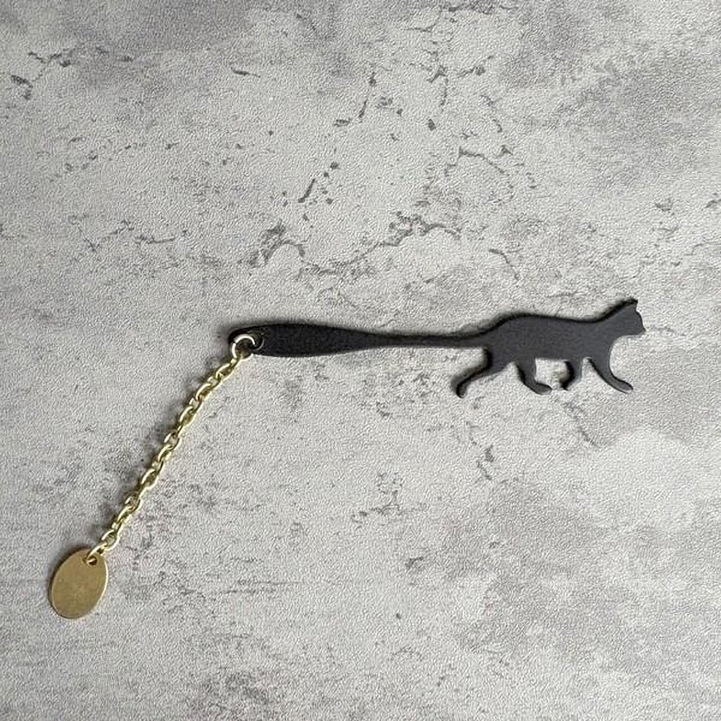 A black cat-shaped keychain with a gold chain attached to it, lying on a textured gray surface.