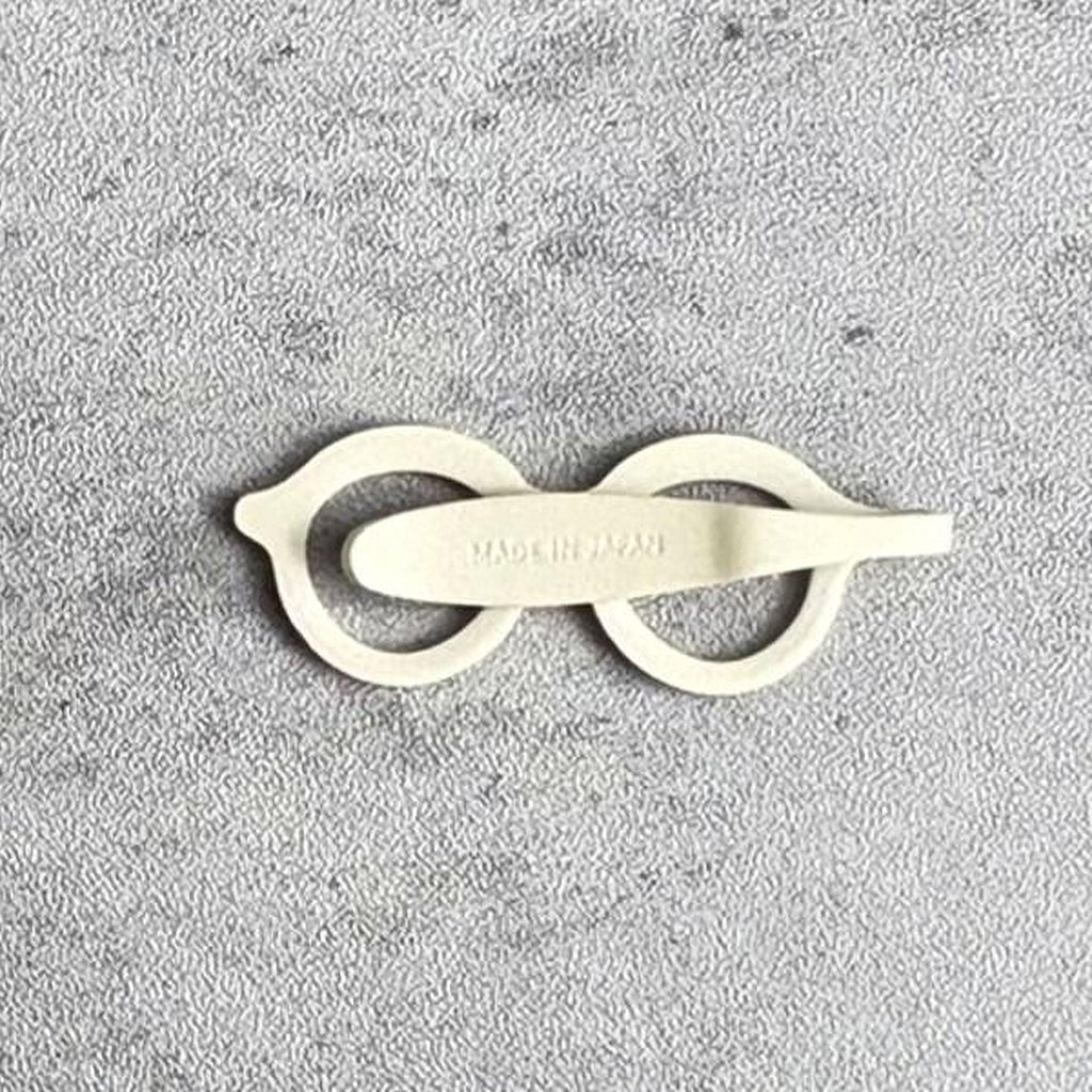 A pair of white glasses with a circular frame and a curved handle, lying on a textured gray surface.
