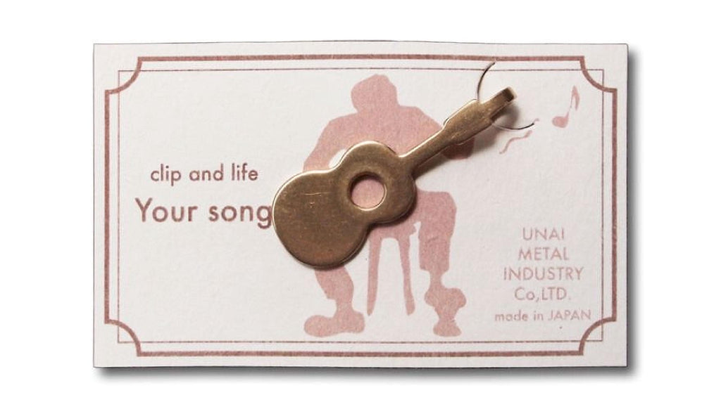 a small golden guitar clip with the text "Your song" on it, placed on a white card with a pink border.