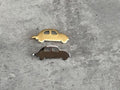 Two small car-shaped charms, one gold and one silver, are placed on a gray surface.