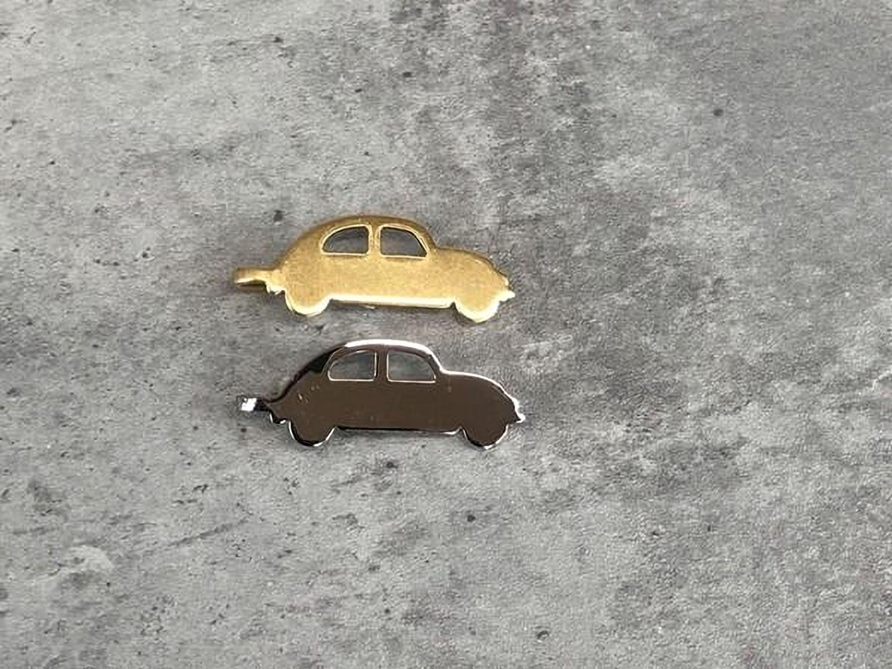 Two small car-shaped charms, one gold and one silver, are placed on a gray surface.