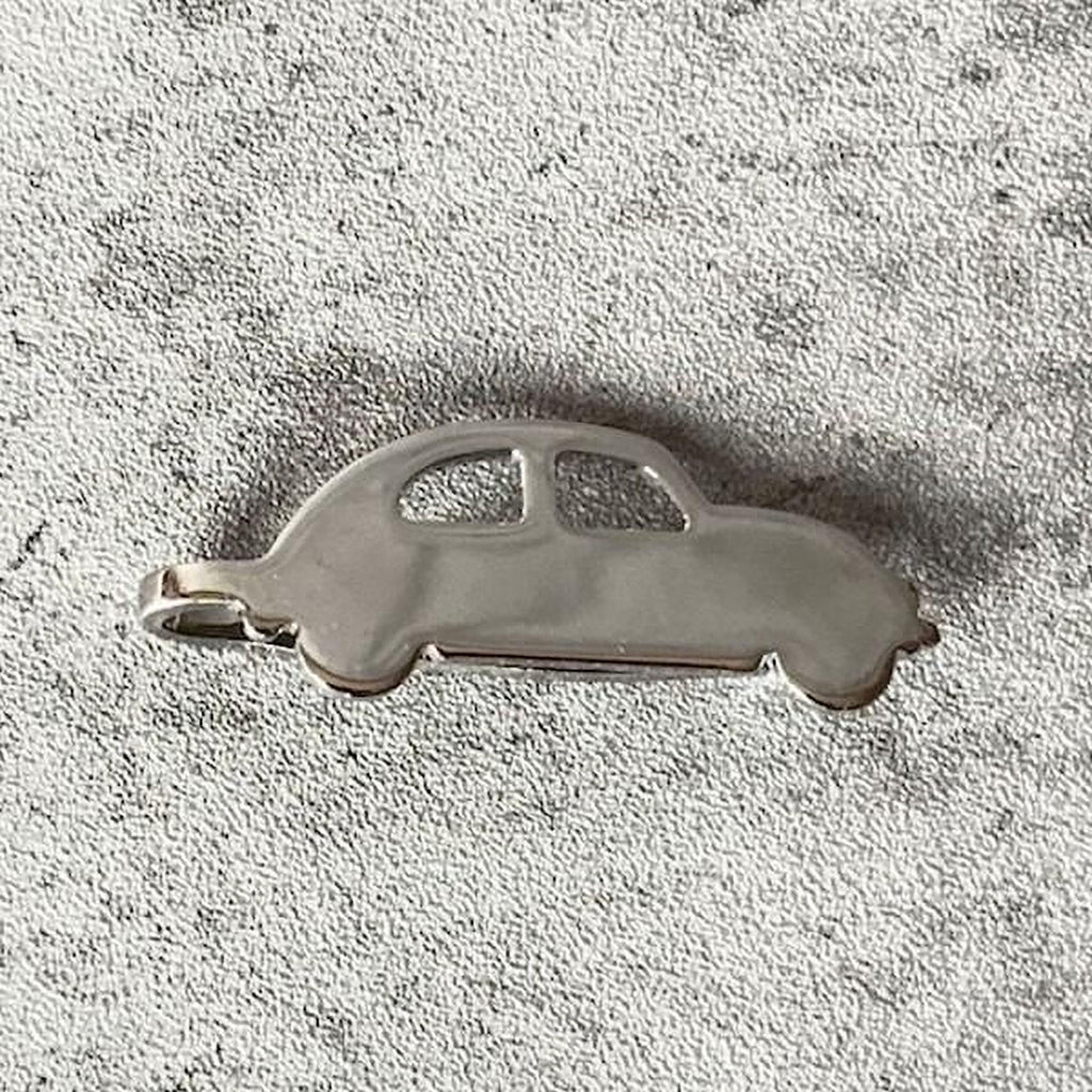 A silver-colored car-shaped pendant or charm is shown against a textured gray background.