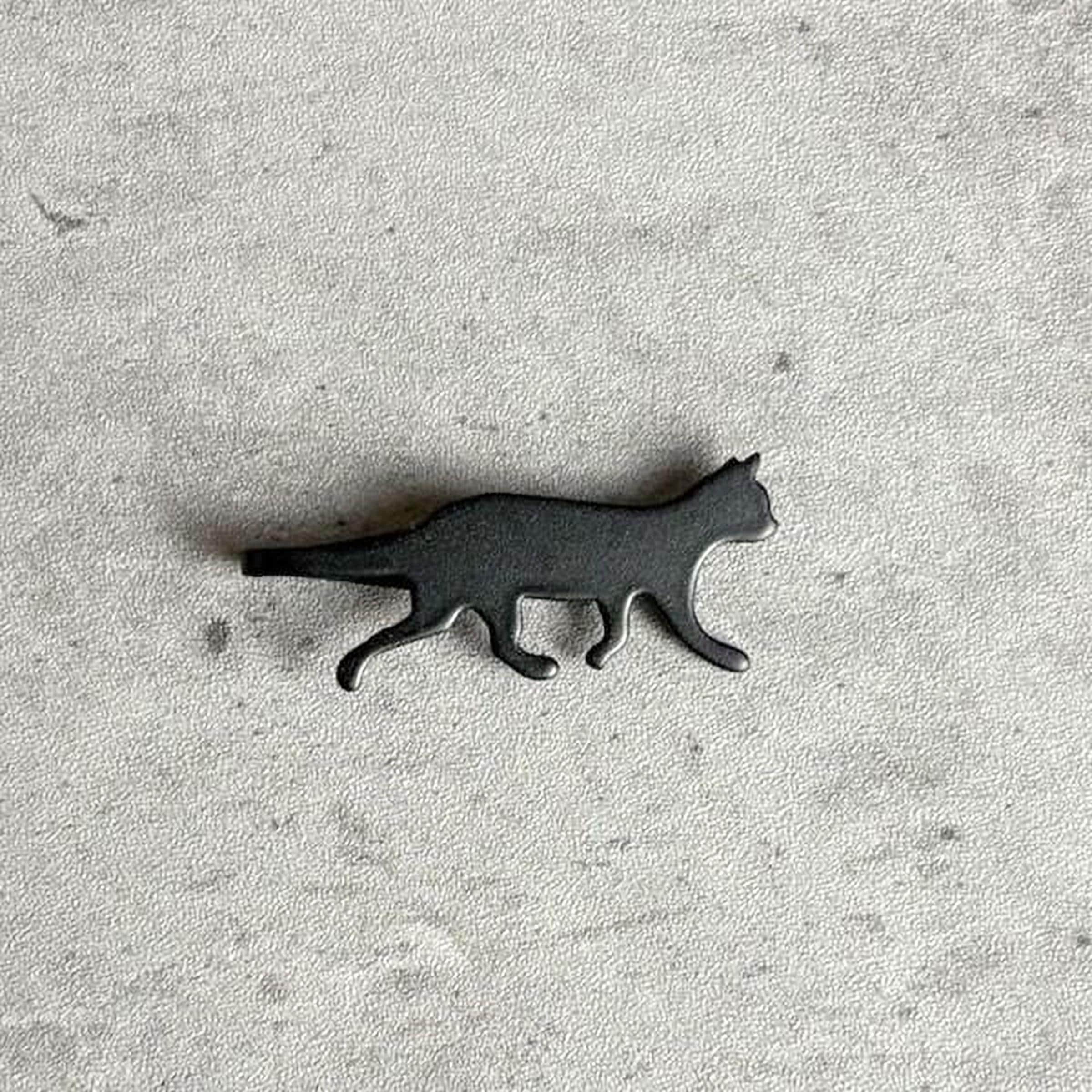 A black cat figurine is shown on a textured gray surface.