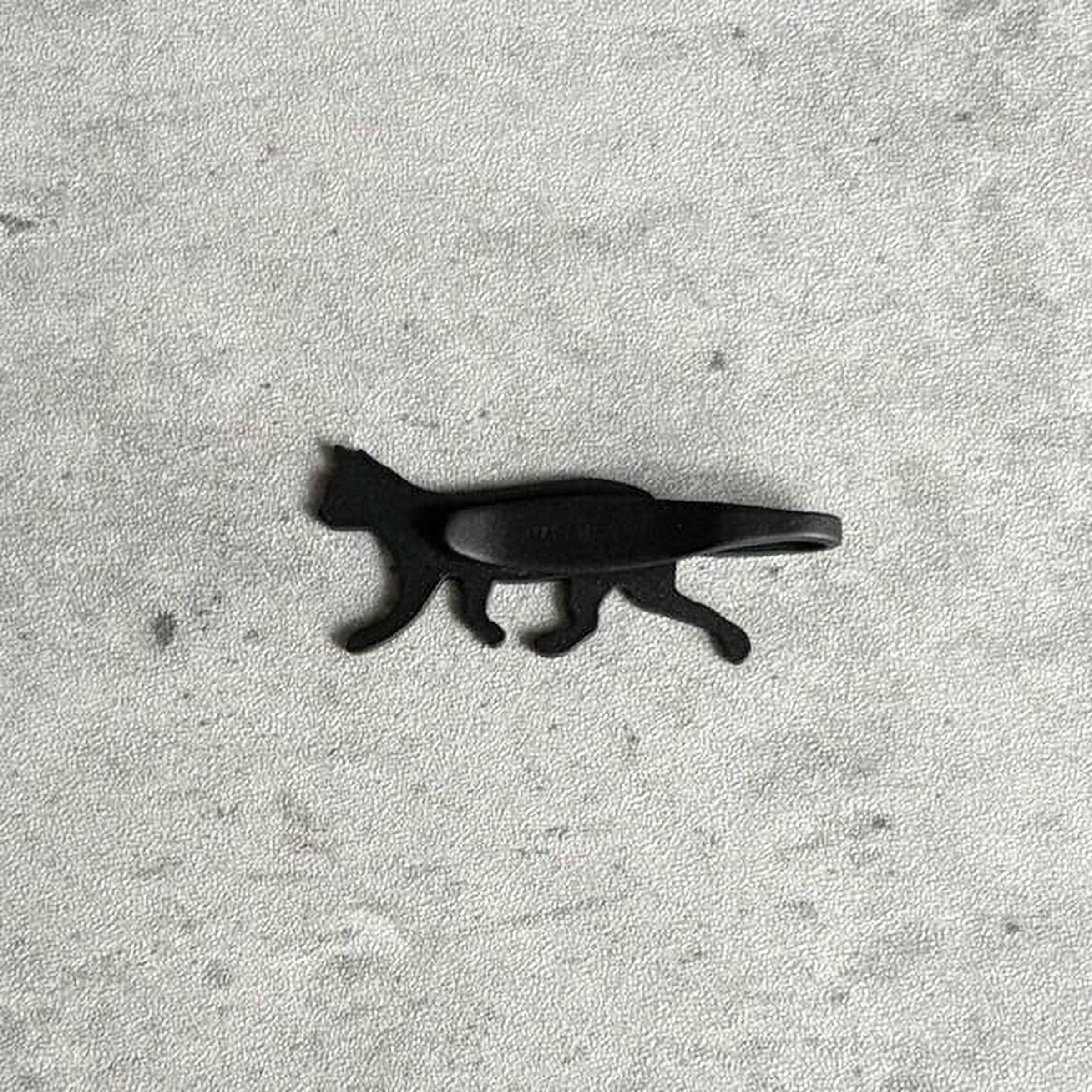 A black cat-shaped object is shown against a textured gray background.