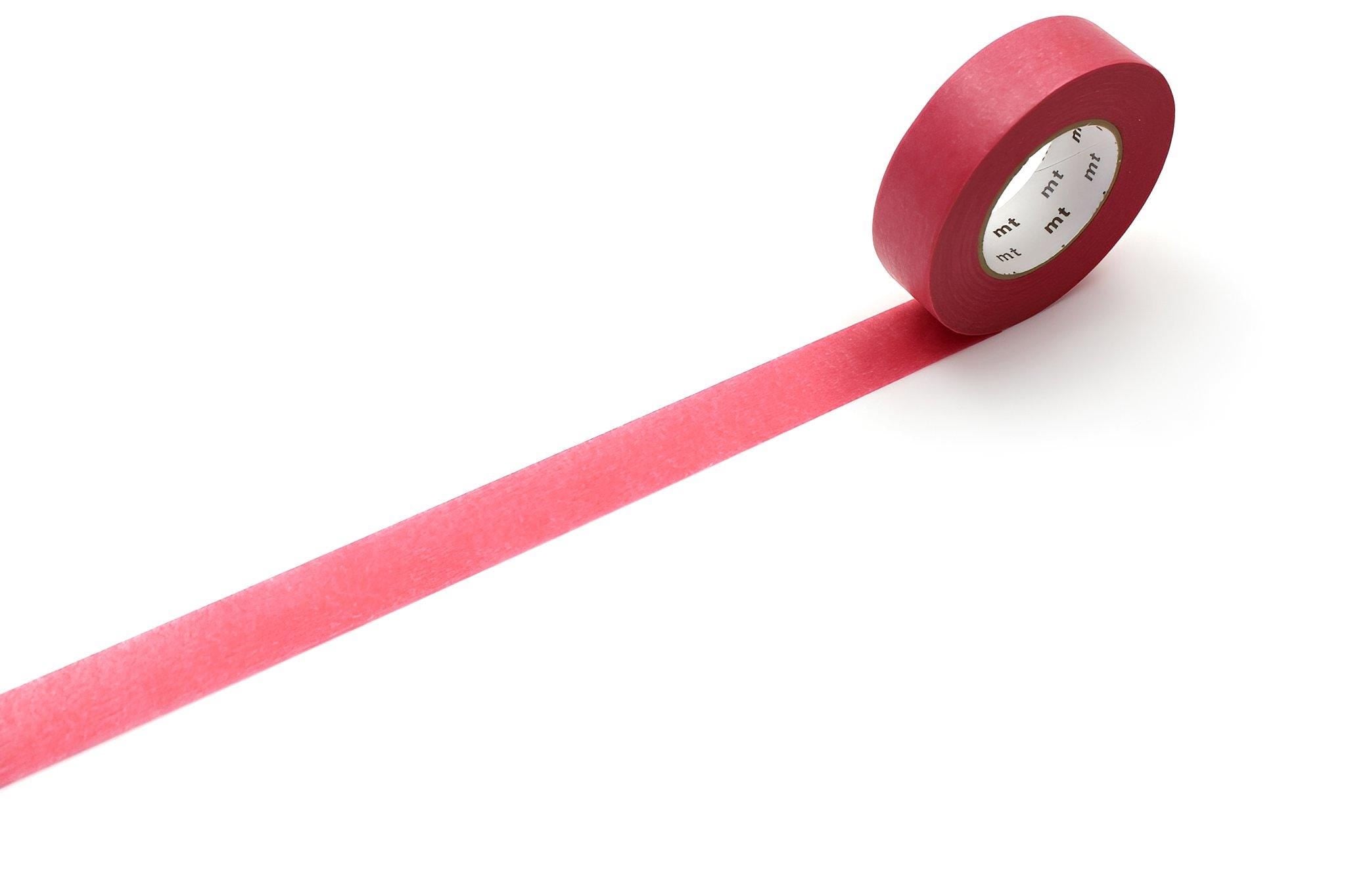A roll of red masking tape is lying on a white surface, with a long red strip extending from the tape.