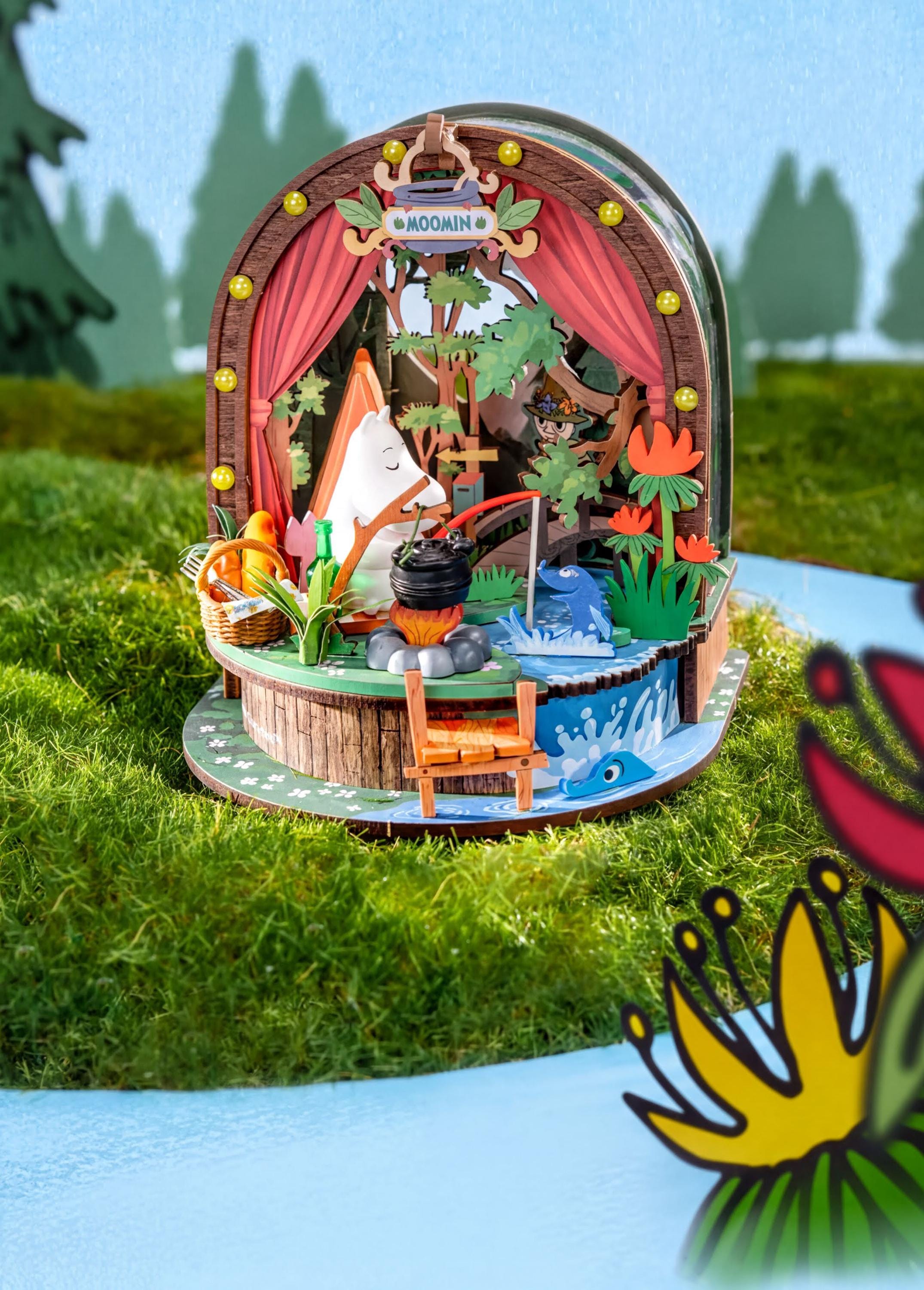A whimsical miniature diorama depicting a forest scene with a pond, a small boat, and various decorative elements such as flowers and a birdhouse.
