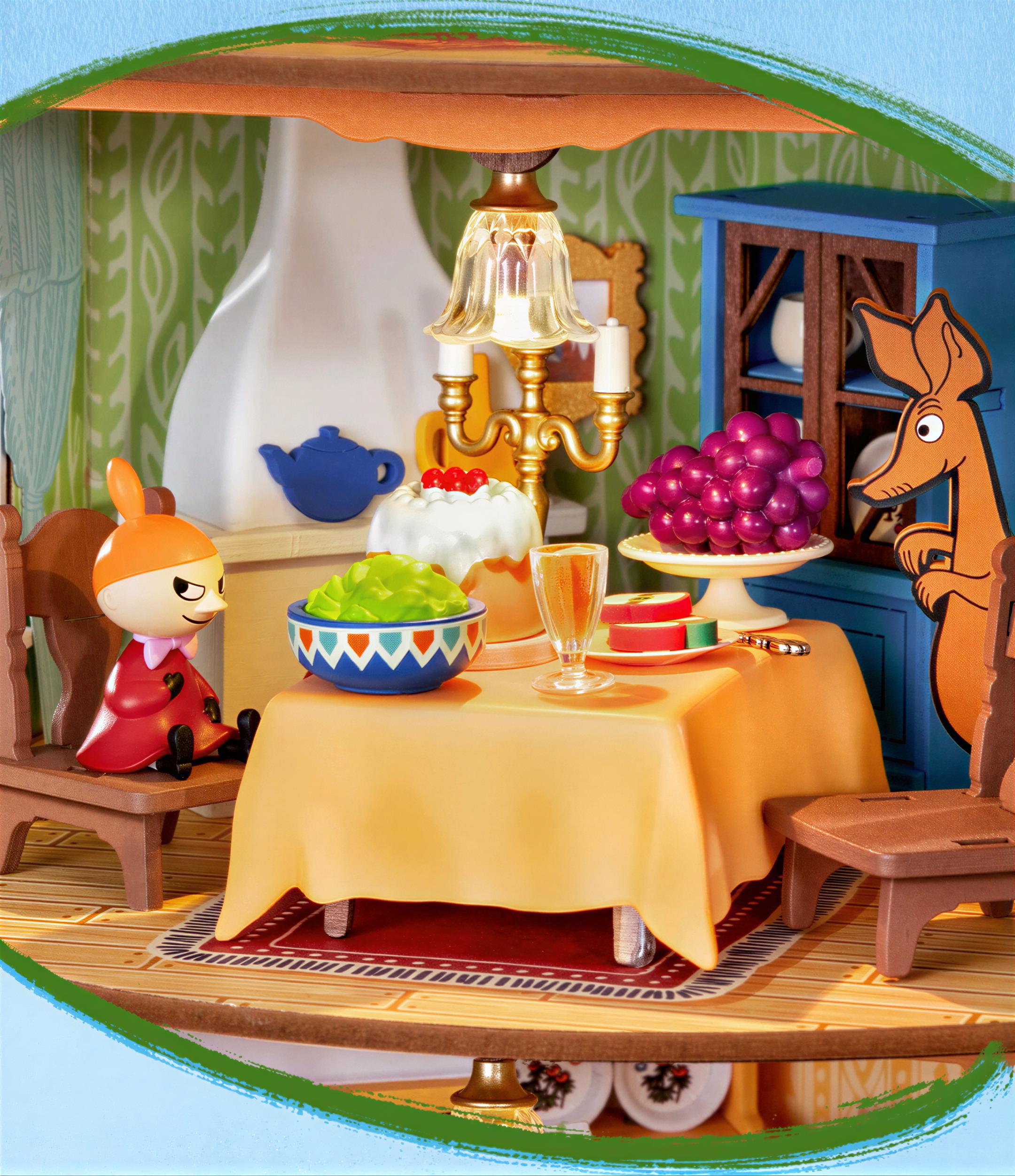 A miniature dollhouse with a table set for a meal, featuring a kangaroo figurine, a teapot, a bowl of fruit, and a cake.