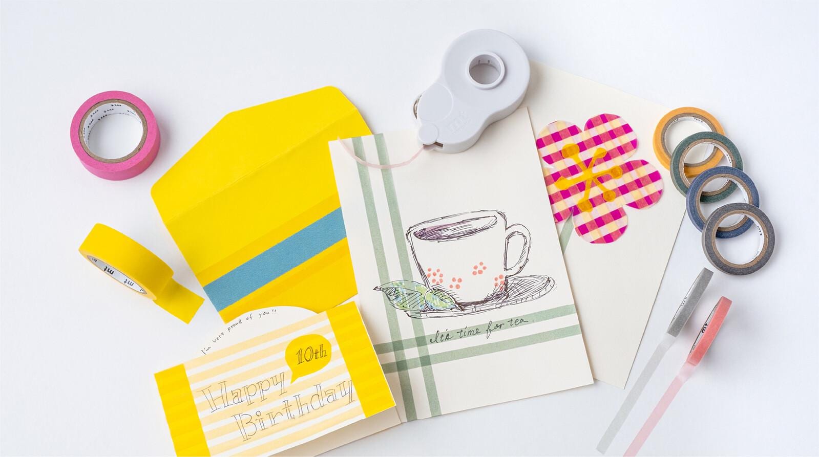 various craft supplies, including a yellow envelope, a white envelope, a cup, and several rolls of tape and markers, all arranged on a white background.