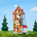 A colorful and detailed dollhouse with multiple levels, set against a backdrop of a grassy hill with pine trees.