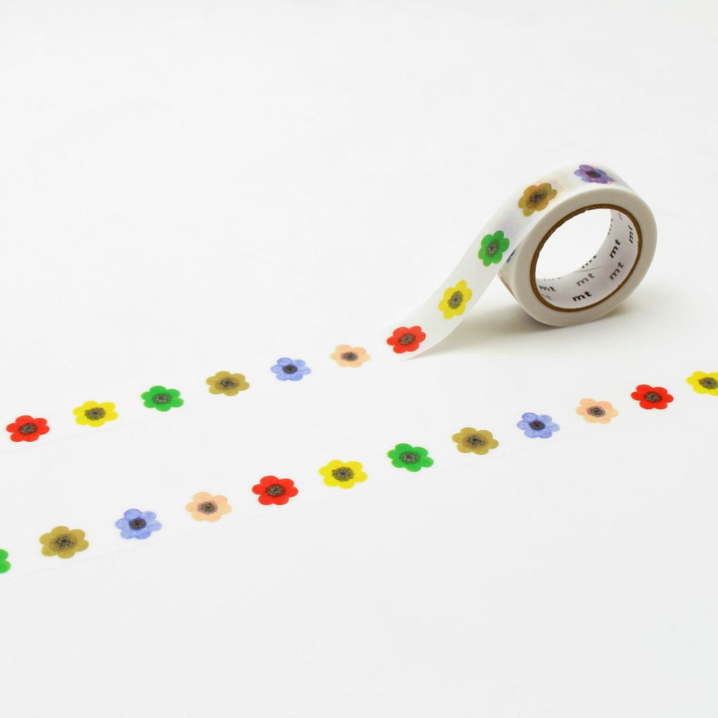 A roll of colorful flower-shaped tape is lying on a white surface, with a row of flower-shaped stickers or decals arranged in a repeating pattern.