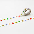 A roll of colorful flower-shaped tape is lying on a white surface, with a row of flower-shaped stickers or decals arranged in a repeating pattern.
