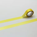 A roll of yellow tape with a white label is lying on a white surface, with the tape partially unrolling and extending across the surface.