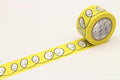 A roll of yellow tape with a repeating pattern of smiling faces on it, placed on a white surface.