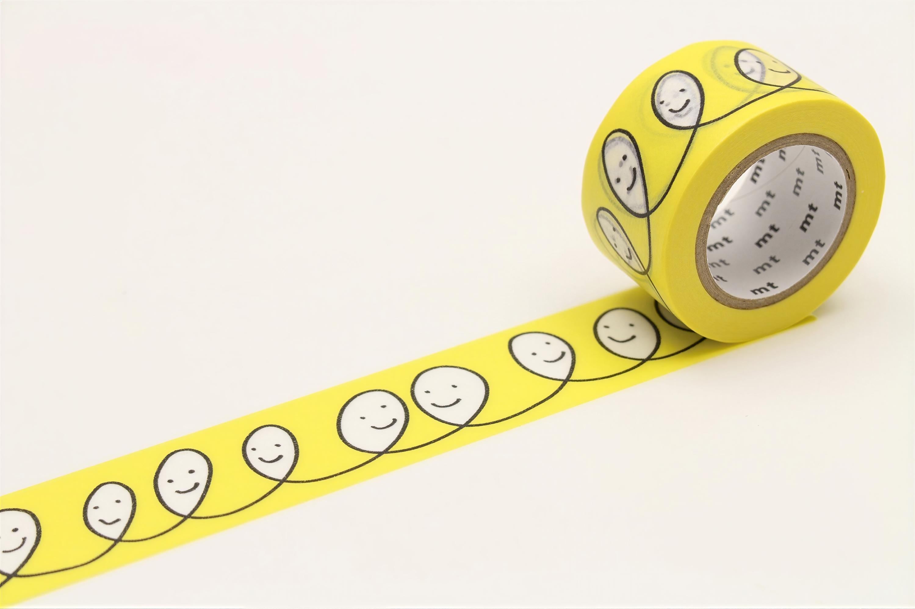 A roll of yellow tape with a repeating pattern of smiling faces on it, placed on a white surface.