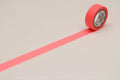 A roll of red tape with a white center is placed on a white surface, with a long pink line extending from the tape.